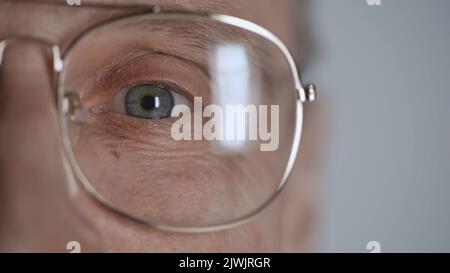 cropped view of mature man with blue eye and eyeglasses looking at camera isolated on grey Stock Photo