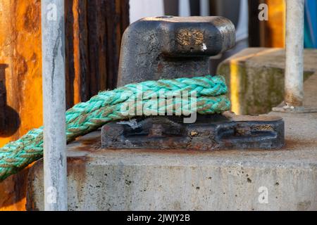 Green rope tied to a metal mooring bollard Stock Photo