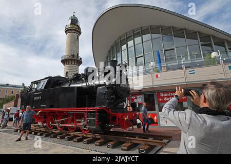 06 September 2022, Mecklenburg-Western Pomerania, Warnemünde: At the start of the Baltic resort's bridge festival, a locomotive of the 'Molli' narrow-gauge railroad stands on Stephan Jantzen Square in front of the lighthouse and the Teepott. The action is to promote the extension of the Molli line of the Mecklenburgische Bäderbahn GmbH to Warnemünde and Rerik. Photo: Bernd Wüstneck/dpa Stock Photo