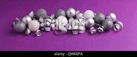 Christmas and New Year ornament on purple background. Silver and white metallic baubles and bows. Banner 16:6 Stock Photo