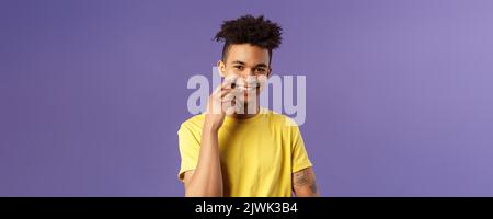 Close-up portrait of lovely young hispanic gay man with dreads, tattoos, touching lip sensually and flirty smiling, checking out someone really cute Stock Photo