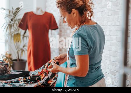 Seamstress at home workshop working with clothes in fashion industry. Professional tailor making dress. Side view of woman in hobby and leisure activi Stock Photo