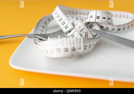 tape measure on plate with fork and knife against orange table background, dieting and loosing weight concept Stock Photo