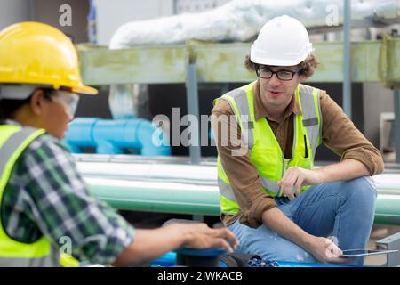 Young woman and man engineer examining pipeline and talking in the factory, mechanic or technician inspector and check plumber valve and discussion to Stock Photo