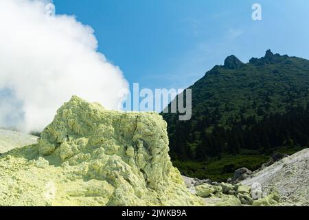 bright smoking fumarole with sulfur deposits against the background of the Mendeleev volcano peak on the island of Kunashir Stock Photo