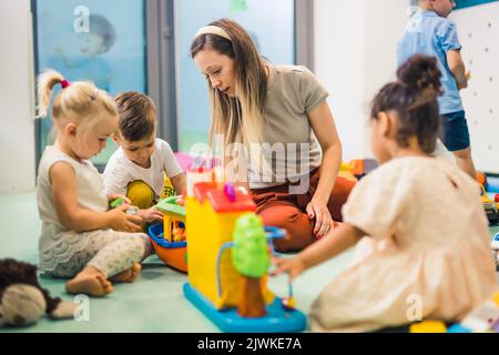 Nursery school. Toddlers and their teacher playing with colorful plastic playhouses, cars and boats. Imagination, creativity, fine motor and gross motor skills development. High quality photo Stock Photo