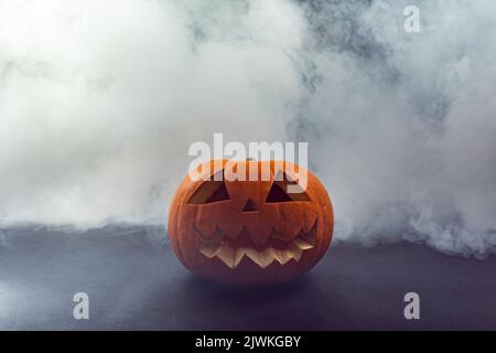 Carved scary halloween pumpkin against smoke effect on grey background Stock Photo