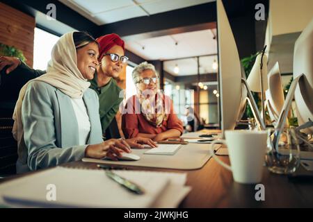 Happy businesswomen having a discussion while looking at a computer screen in an office. Multicultural businesswomen working as a team in a modern co- Stock Photo