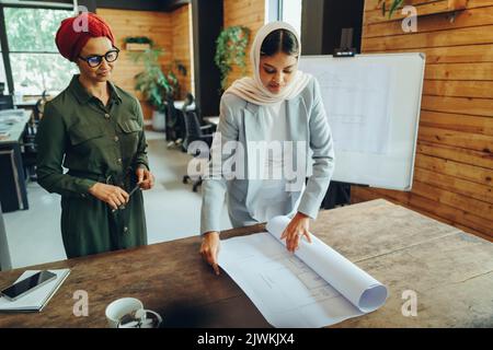 Two Muslim architects working with blueprint drawings in a modern office. Two creative businesswomen planning an innovative project. Female designers Stock Photo