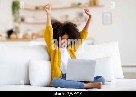 Happy african american child using laptop, raising hands up Stock Photo
