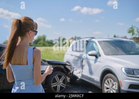 Stressed woman driver standing on street side shocked after car accident. Road safety and insurance concept Stock Photo