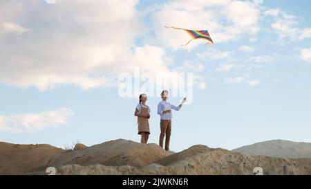 Brother and sister fly a kite into the sky on a high mountain. Stock Photo