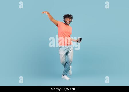Happy eastern guy using wireless headset and smartphone, dancing Stock Photo