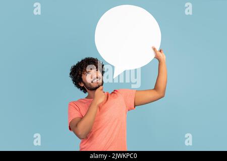 Pensive indian man holding blank speech bubble on blue, thinking Stock Photo