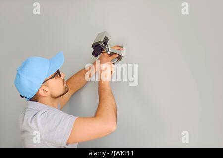 Company security specialist man mounts surveillance camera for CCTV system on wall inside building Stock Photo