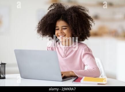 Adorable black girl doing homework, using laptop Stock Photo