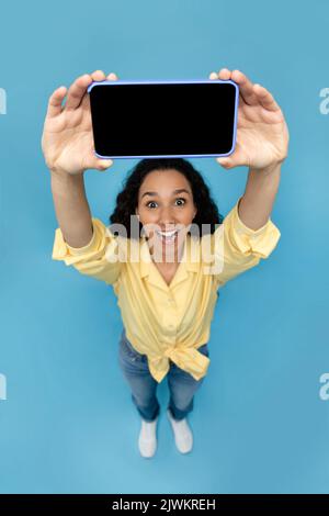Young woman holding smartphone with blank screen, presenting gadget with free space for mockup, recommending mobile app Stock Photo