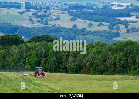 Red Massey Ferguson 7719 S tractor & Claas Disco 3200c swathing hay - hillside farmland pasture, scenic Wharfedale countryside, Yorkshire, England UK. Stock Photo