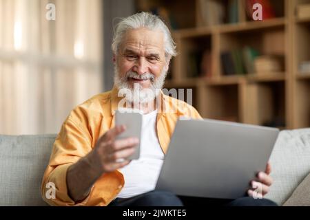 happy old man using smartphone and laptop at home Stock Photo