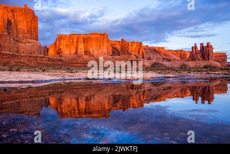 The Three Gossips reflected in an ephemeral rainwater pool in the Courthouse Towers section, Arches National Park, Moab, Utah. Stock Photo