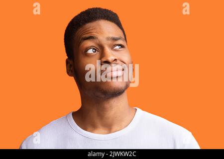 Portrait Of African Guy Having Doubt Looking Aside, Orange Background Stock Photo
