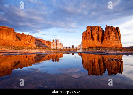 The Three Gossips, Sheep Rock and the Organ reflected in an ephemeral rainwater pool in Arches National Park, Moab, Utah.  Courthouse Towers Section. Stock Photo