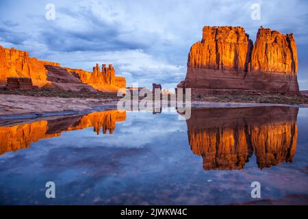 The Three Gossips, Sheep Rock and the Organ reflected in an ephemeral rainwater pool in Arches National Park, Moab, Utah.  Courthouse Towers Section. Stock Photo