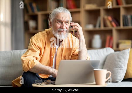 Cheerful elderly man using laptop, having phone conversation Stock Photo