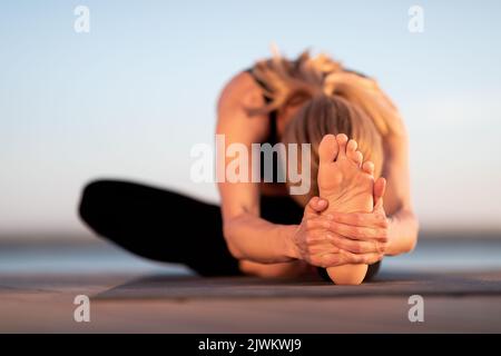 Flexible young woman stretching while practicing yoga outdoors Stock Photo