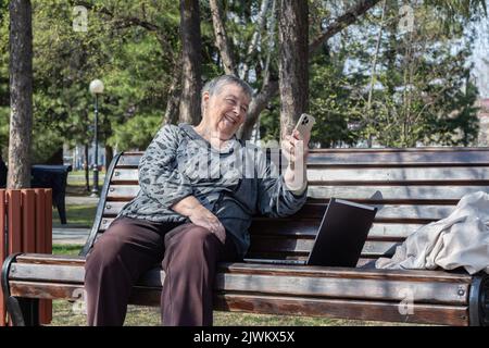 Portrait of senior womane injoying pleasant conversation on mobile phone  with laptop in city park, relaxing outdoors. selective focus. Grandparents d Stock Photo