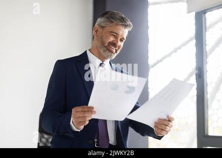 Happy Middle Aged Entrepreneur Reading Business Papers At Office Stock Photo