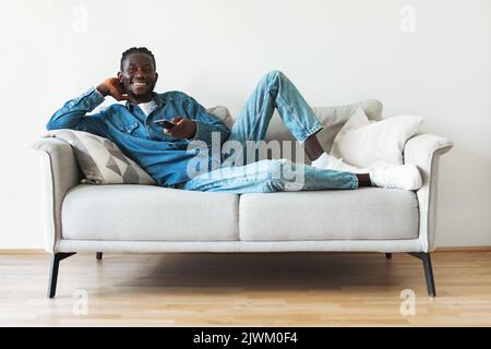 Happy Black Guy Watching Television Lying On Sofa At Home Stock Photo