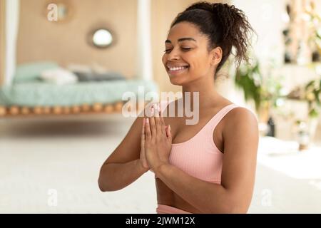 Concentration concept. Happy african american lady with closed eyes holding hands in prayer pose, meditating and smiling Stock Photo