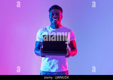 Check this website. Handsome young black man holding laptop with blank screen in neon light, mockup for design Stock Photo