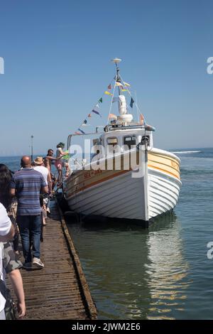 Tourists queue on the jetty to board the Sea Jay pleasure boat for trips around Llandudno's North Shore, Great Orme and Pier on a sunny summer day Stock Photo