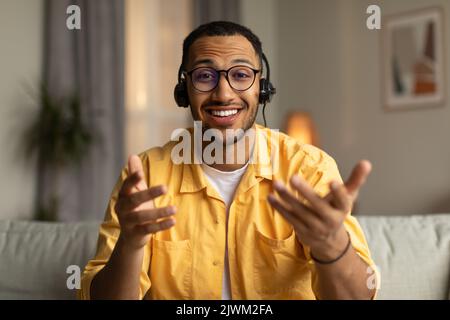Young African American guy in headphones having online meeting, participating in webinar or business conference at home Stock Photo