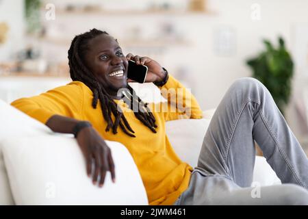 Positive Black Man Talking On Cellphone While Relaxing On Couch At Home Stock Photo