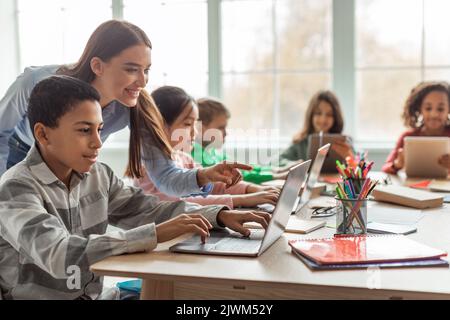 Teacher Teaching Diverse School Kids Using Laptop In Classroom Stock Photo