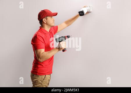 Worker holding a drilling machine and installing a security camera on a wall Stock Photo