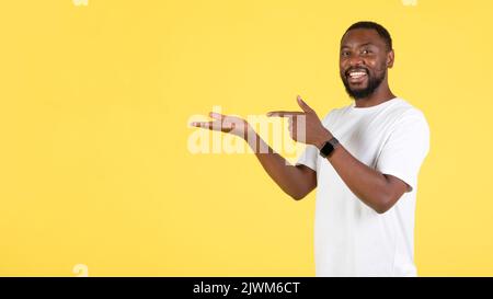 Black Guy Pointing At Hand Holding Invisible Object, Yellow Background Stock Photo