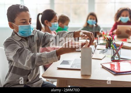 African American Schoolboy Using Sanitizer Disinfecting Hands In Classroom Stock Photo