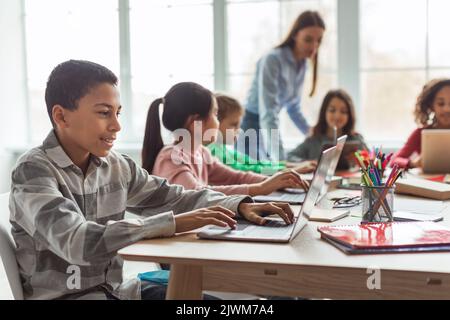 Cheerful Black Schoolboy Using Laptop Computer Learning Online In Classroom Stock Photo