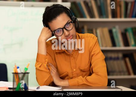 Portrait of exhausted mixed race female teacher feeling tired after virtual online meeting, sitting in library Stock Photo