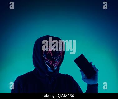 Digital security Concept. Anonymous hacker with mask holding smartphone hacked. Personal and Cyber data security in mobile phone stolen by man in mask Stock Photo