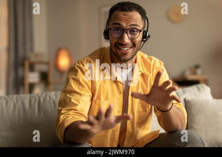 Positive young black guy in headphones video conferencing online, having webinar or business meeting at home office Stock Photo