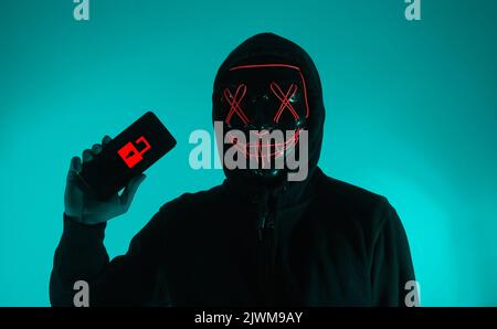 Digital security Concept. Anonymous hacker with mask holding smartphone hacked. Personal and Cyber data security in mobile phone stolen by man in mask Stock Photo