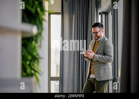Surprised young adult businessman, standing in the hall, scrolling through his phone. Stock Photo