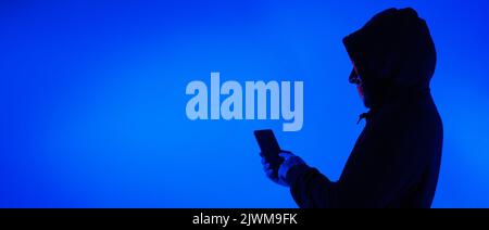 Digital security Concept. Anonymous hacker with mask holding smartphone hacked. Personal and Cyber data security in mobile phone stolen by man in mask Stock Photo