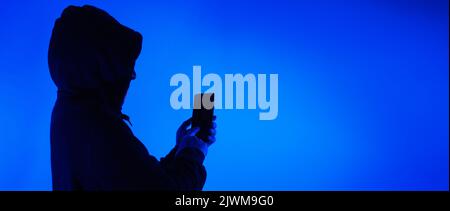 Digital security Concept. Anonymous hacker with mask holding smartphone hacked. Personal and Cyber data security in mobile phone stolen by man in mask Stock Photo