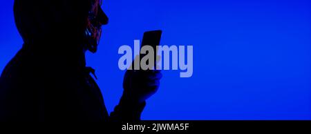 Digital security Concept. Anonymous hacker with mask holding smartphone hacked. Personal and Cyber data security in mobile phone stolen by man in mask Stock Photo